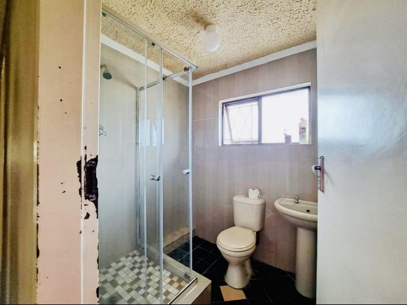 A functional bathroom featuring a glass shower enclosure, pedestal sink, and toilet, with tiled finishes throughout.