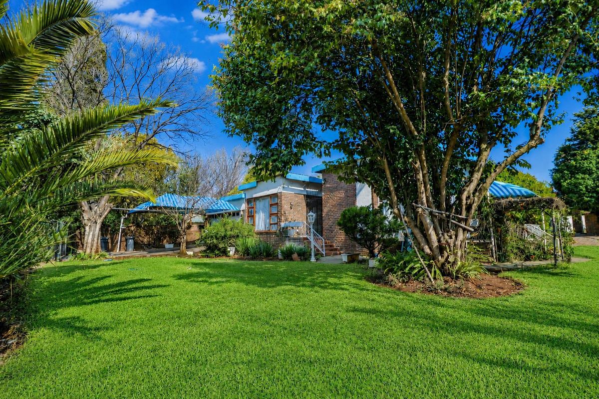 A view of the rear garden and brick facade of the house, featuring established trees, a lawn, and covered patio areas.