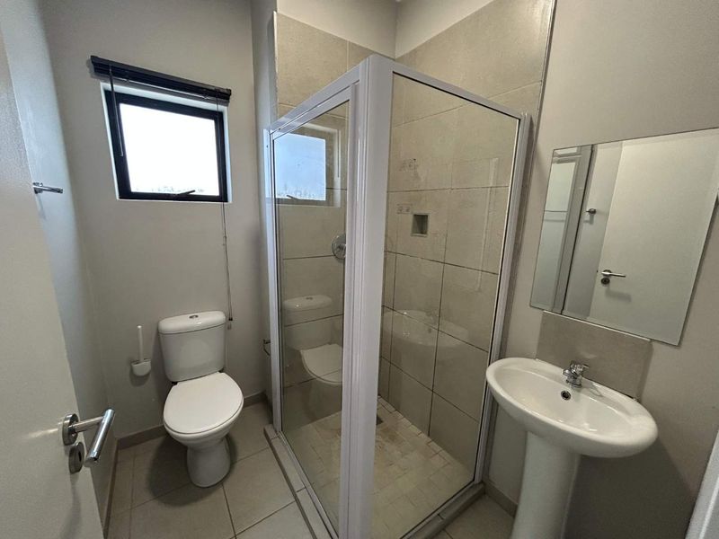 A functional bathroom featuring a pedestal basin, a glass-enclosed shower, and neutral wall and floor tiling.