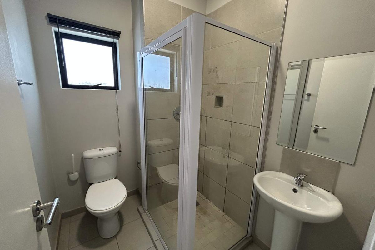 A functional bathroom featuring a pedestal basin, a glass-enclosed shower, and neutral wall and floor tiling.