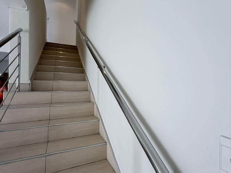 A clean, modern staircase featuring tiled steps and a sleek stainless steel handrail, providing access between levels in the townhouse.