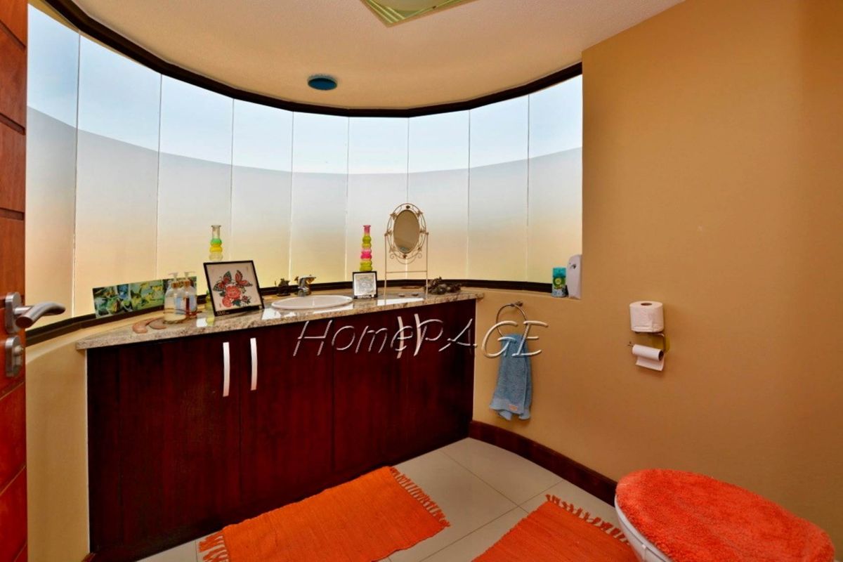 A bathroom featuring a curved vanity with granite countertop, integrated sink, and dark wood cabinetry, set against a large curved window.