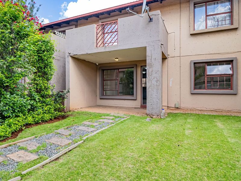 Rear view of the apartment featuring a covered patio, a small balcony above, and a private garden area with a paved walkway.