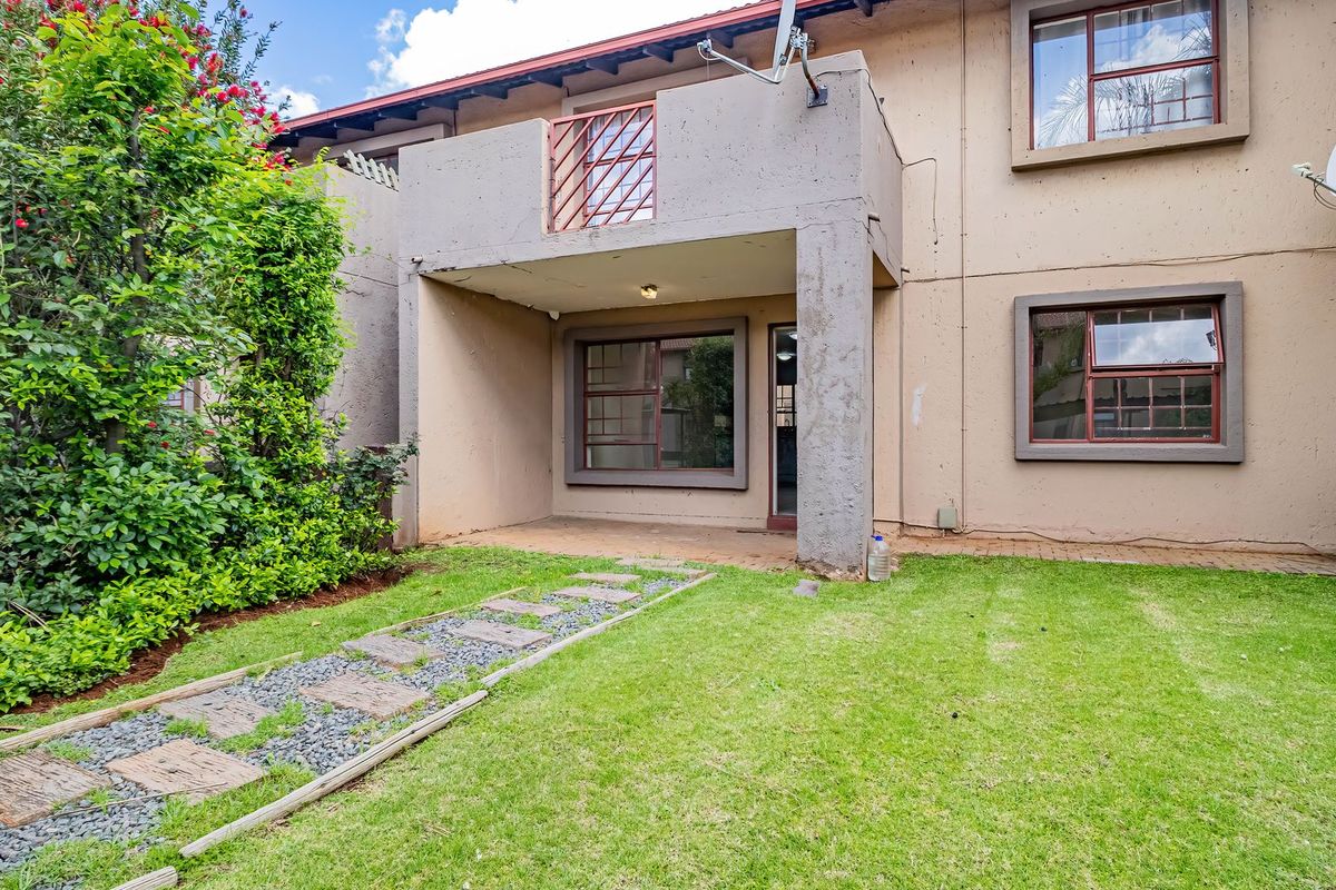 Rear view of the apartment featuring a covered patio, a small balcony above, and a private garden area with a paved walkway.