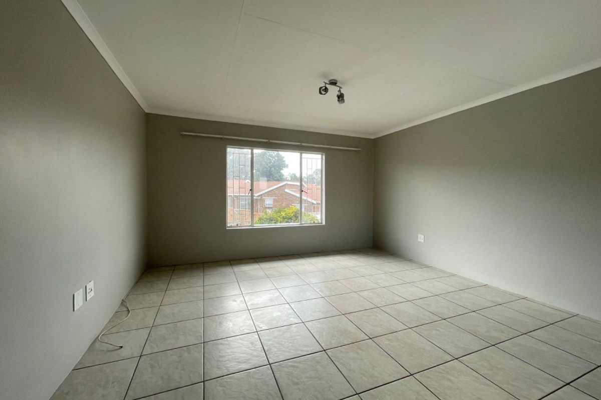 A spacious, empty bedroom featuring neutral wall paint, tiled flooring, and a large window with security bars, offering a clean canvas for personalization.
