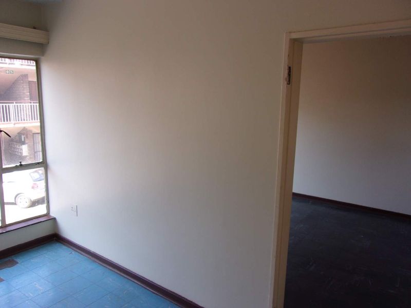 An empty bedroom featuring tiled flooring and a doorway leading to an adjacent room, with natural light provided by a side window.