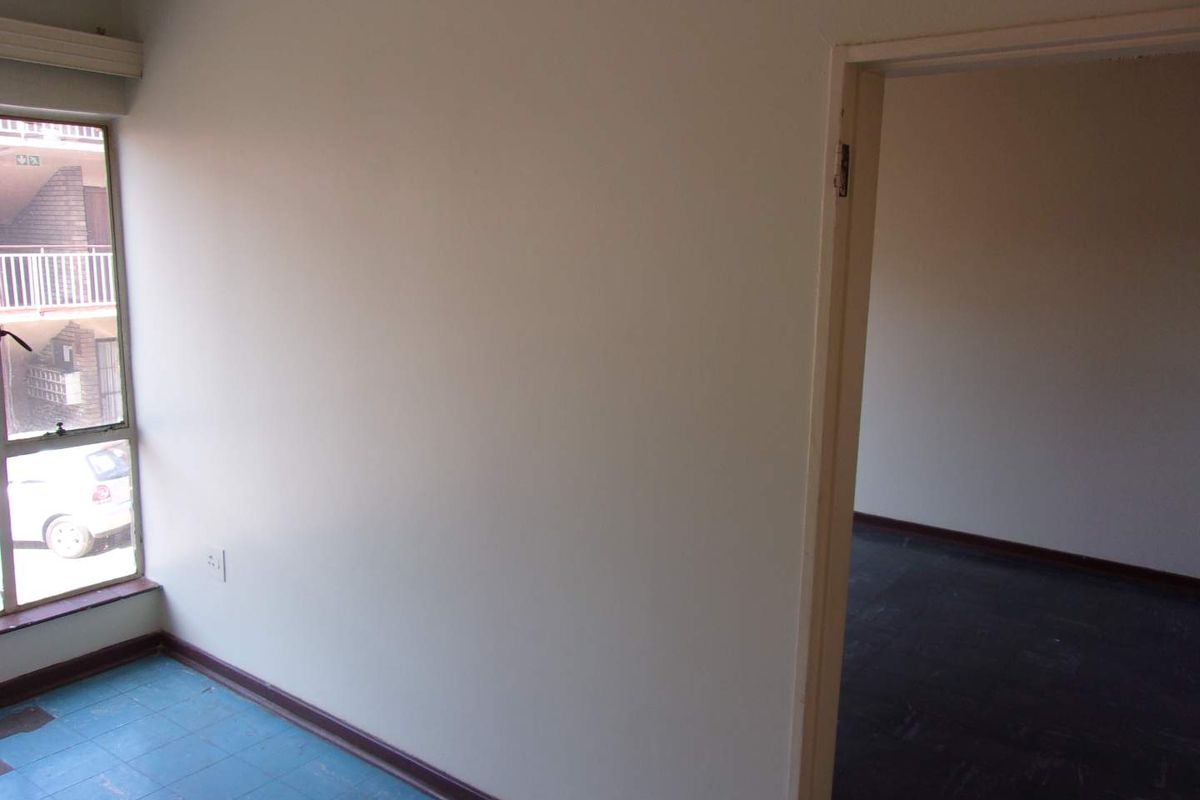 An empty bedroom featuring tiled flooring and a doorway leading to an adjacent room, with natural light provided by a side window.