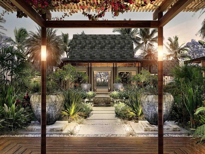 A beautifully landscaped rear garden featuring a timber pergola, stone pathway, central water feature, and lush tropical plantings leading to the main residence.