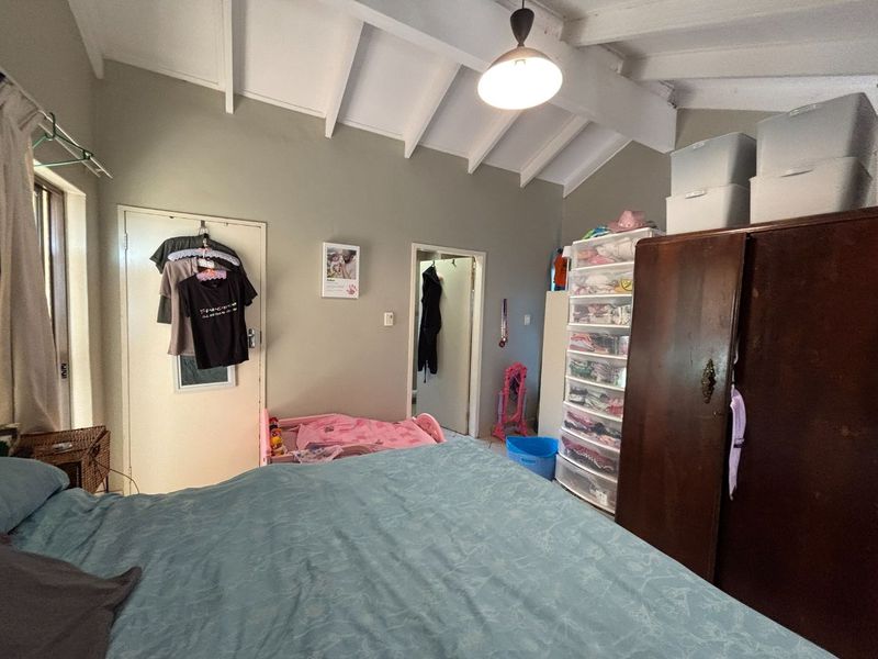 A bedroom featuring a vaulted ceiling with exposed timber beams and a central pendant light fixture.