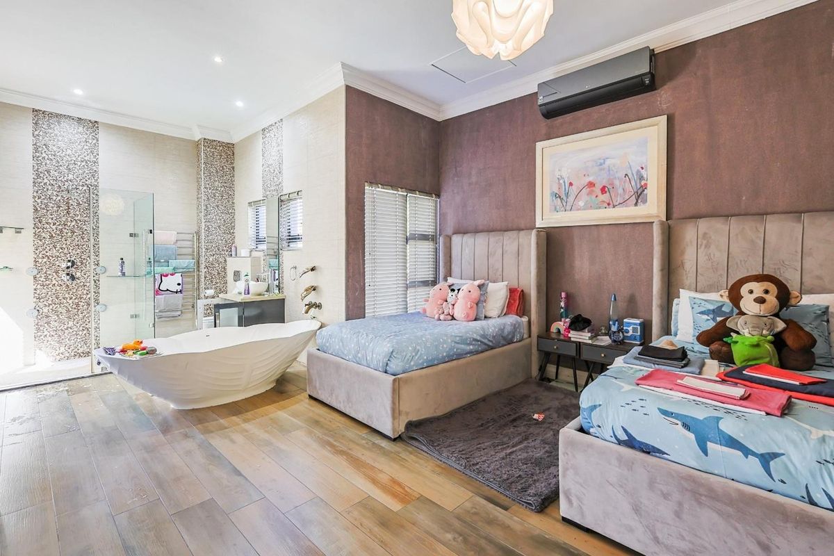 A spacious bedroom featuring an integrated open-plan bathroom with a freestanding bathtub, glass-enclosed shower, and modern wood-look flooring.