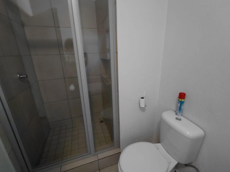 A functional bathroom featuring a glass-enclosed shower with tiled walls and a standard toilet.