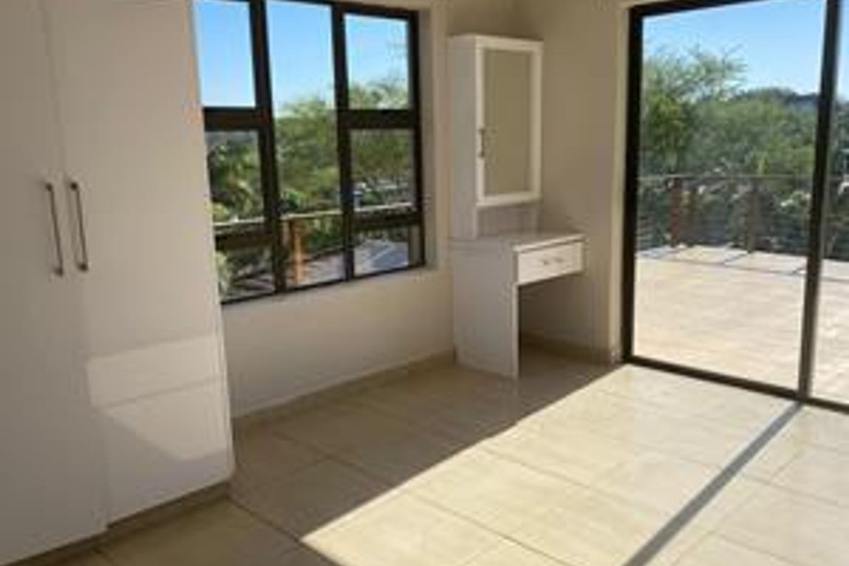 Bright bedroom featuring built-in cabinetry, tiled flooring, and large sliding glass doors opening onto an outdoor balcony with scenic views.