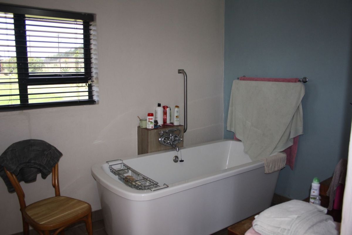 A functional bathroom featuring a freestanding bathtub with a wall-mounted grab rail and a window with fitted blinds.