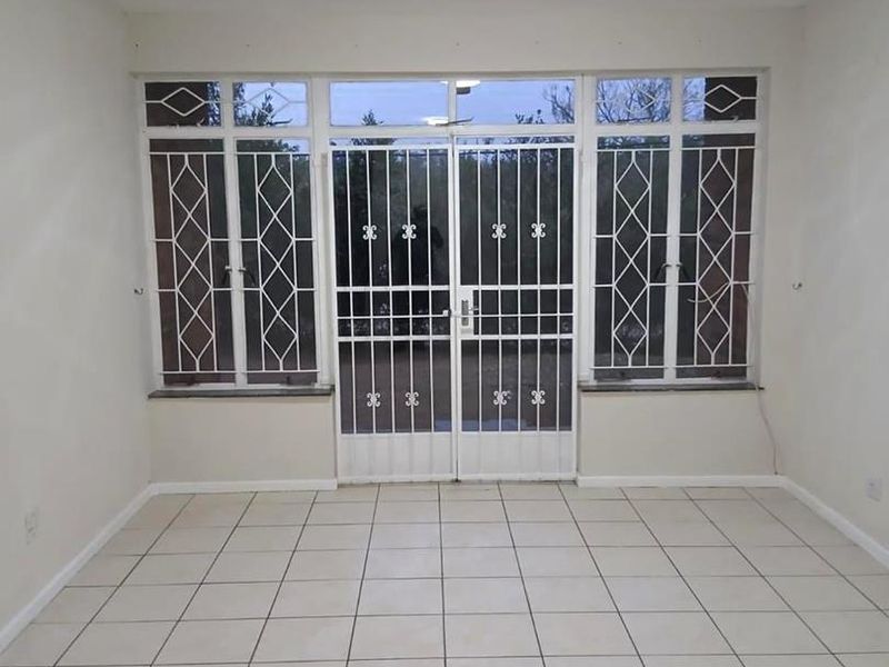 An empty living room featuring neutral tiled flooring, a central ceiling light, and secure metal security gates and window bars.