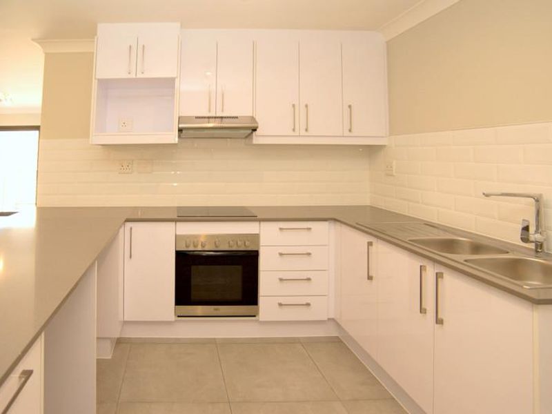 Modern kitchen featuring white cabinetry, stone countertops, subway tile backsplash, built-in oven, electric cooktop, and a double bowl sink with mixer tap.