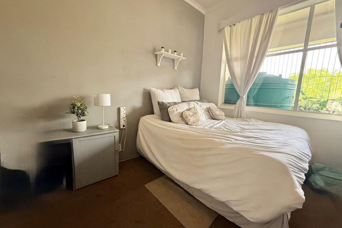 A bedroom featuring a large window with security bars, neutral wall tones, and carpeted flooring.