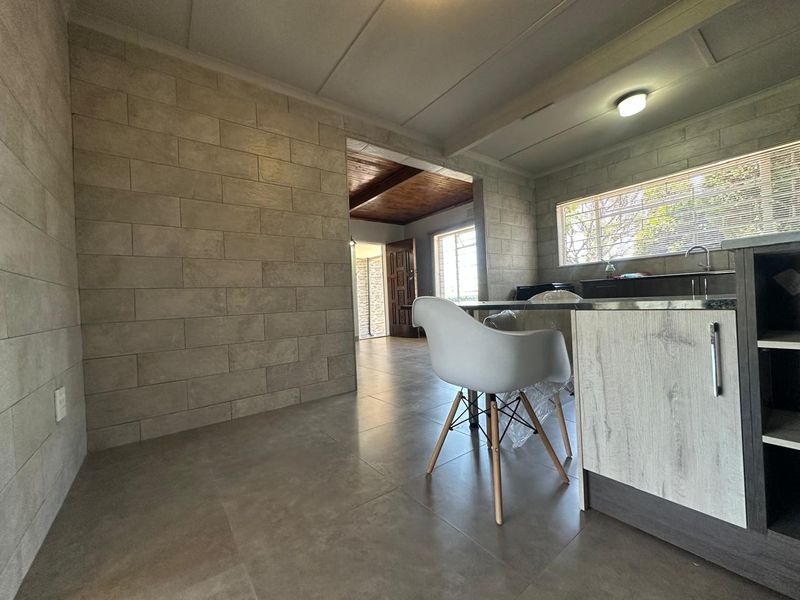 Open plan living and kitchen area featuring modern tiled flooring, stone-look wall cladding, and functional kitchen cabinetry with a sink.