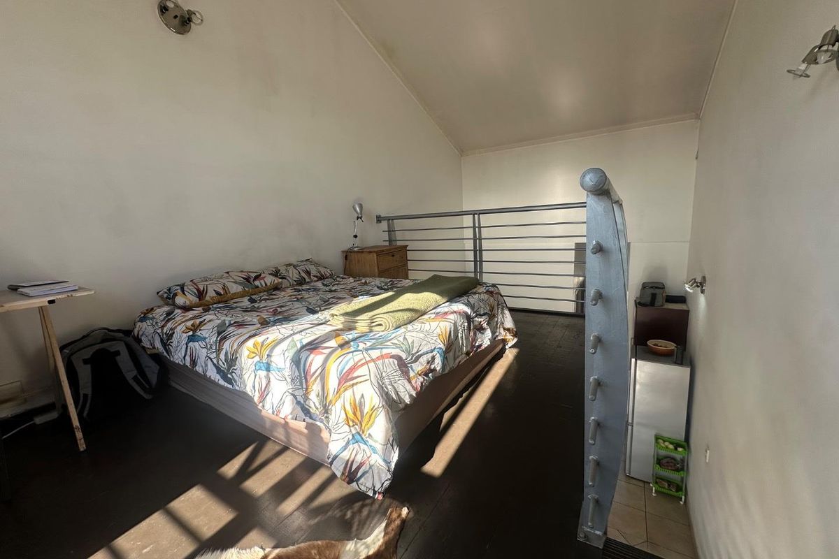 A loft-style bedroom featuring dark timber flooring, a metal safety balustrade, and a sloped ceiling with wall-mounted lighting.