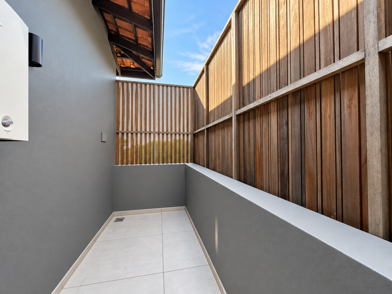 A clean, modern outdoor balcony area featuring tiled flooring, a timber privacy screen, and a wall-mounted gas water heater.