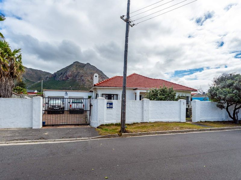 Front elevation of a single-story house featuring a tiled roof, perimeter wall with a metal gate, and mountain views.