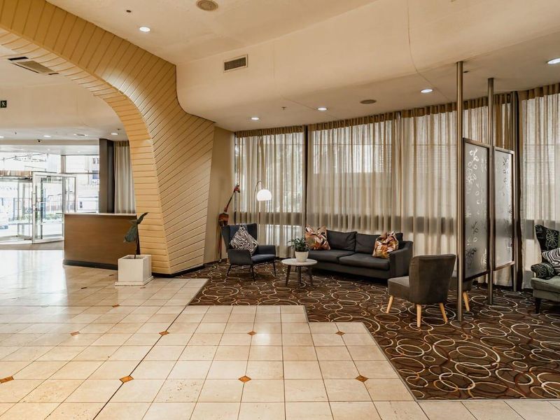 Spacious apartment building lobby featuring a reception area, decorative architectural archway, tiled and carpeted flooring, and large windows with privacy curtains.