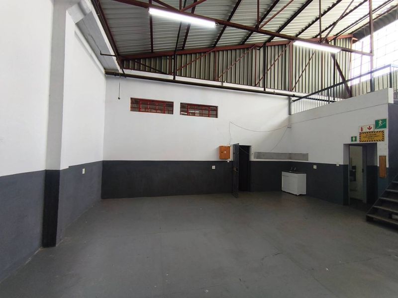 Spacious industrial utility area featuring high ceilings with exposed steel trusses, concrete flooring, a mezzanine level, and a functional sink unit.