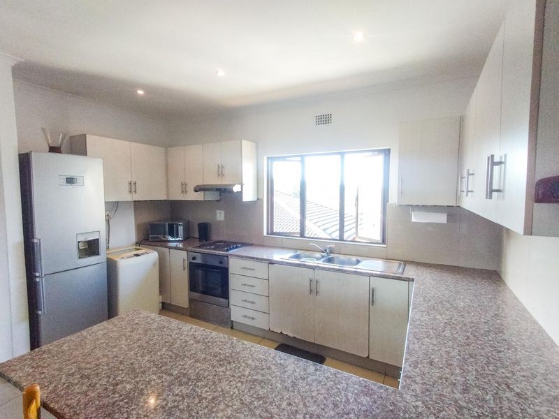Functional kitchen featuring granite countertops, ample built-in cabinetry, stainless steel sink, and integrated oven with extractor fan.