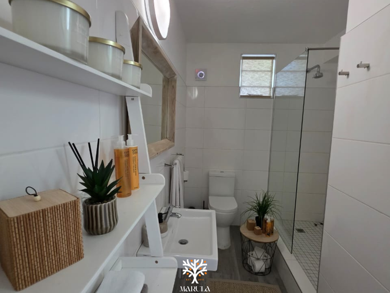 Modern bathroom featuring a walk-in shower with glass screen, wall-mounted basin, toilet, and clean white wall tiling.