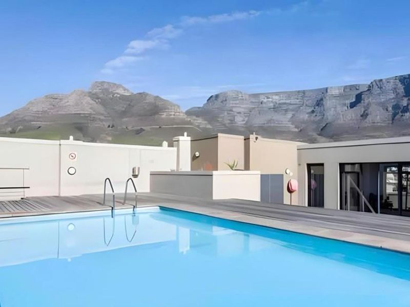 A well-maintained rooftop swimming pool area featuring timber decking and stunning mountain views.