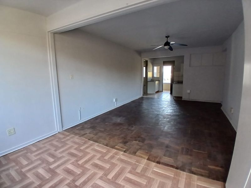 An open-plan living and kitchen area featuring parquet flooring, a ceiling fan, and direct access to a kitchen space with built-in cabinetry.