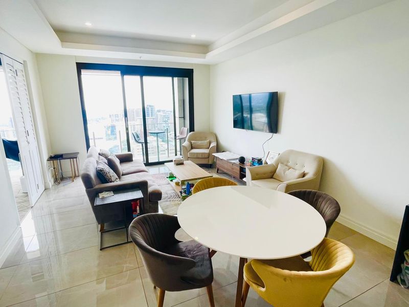 Spacious open-plan living and dining area featuring large sliding glass doors that open to a balcony with city views and modern tiled flooring.