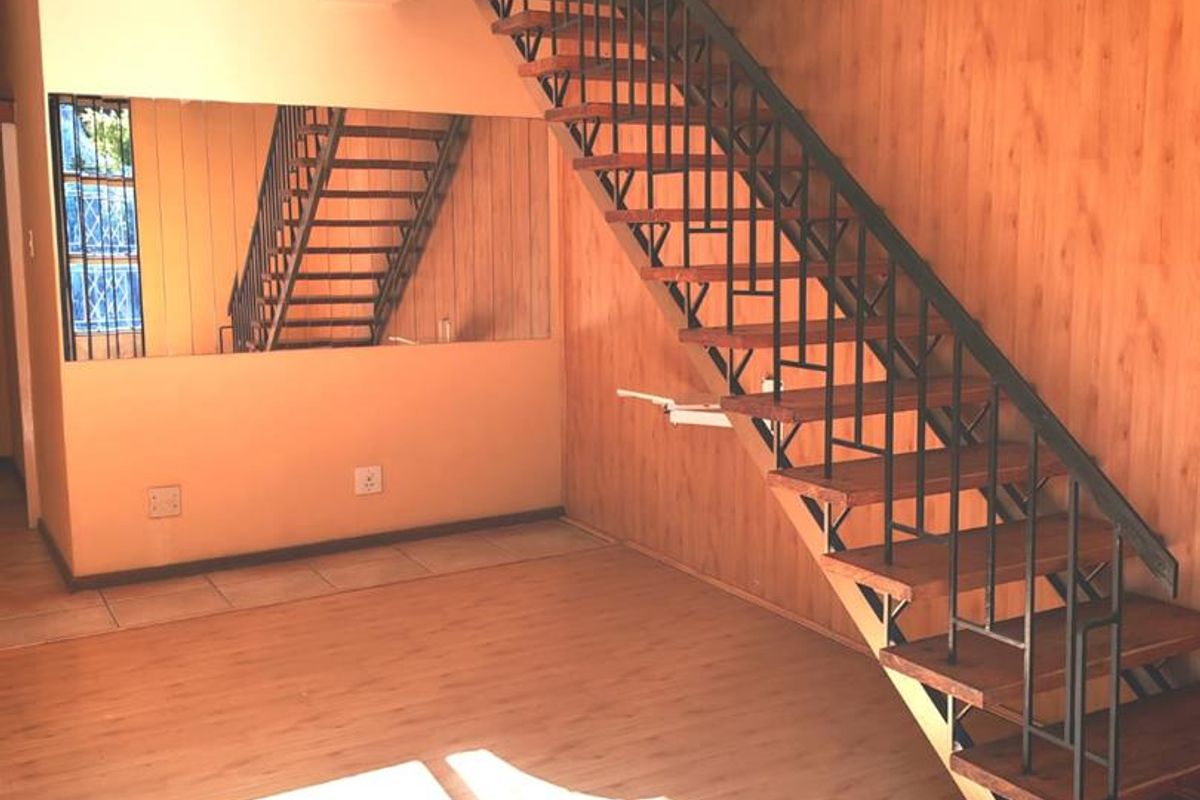 An open-plan living area featuring a distinctive open-tread staircase with metal balustrades and wood-panelled wall accents.