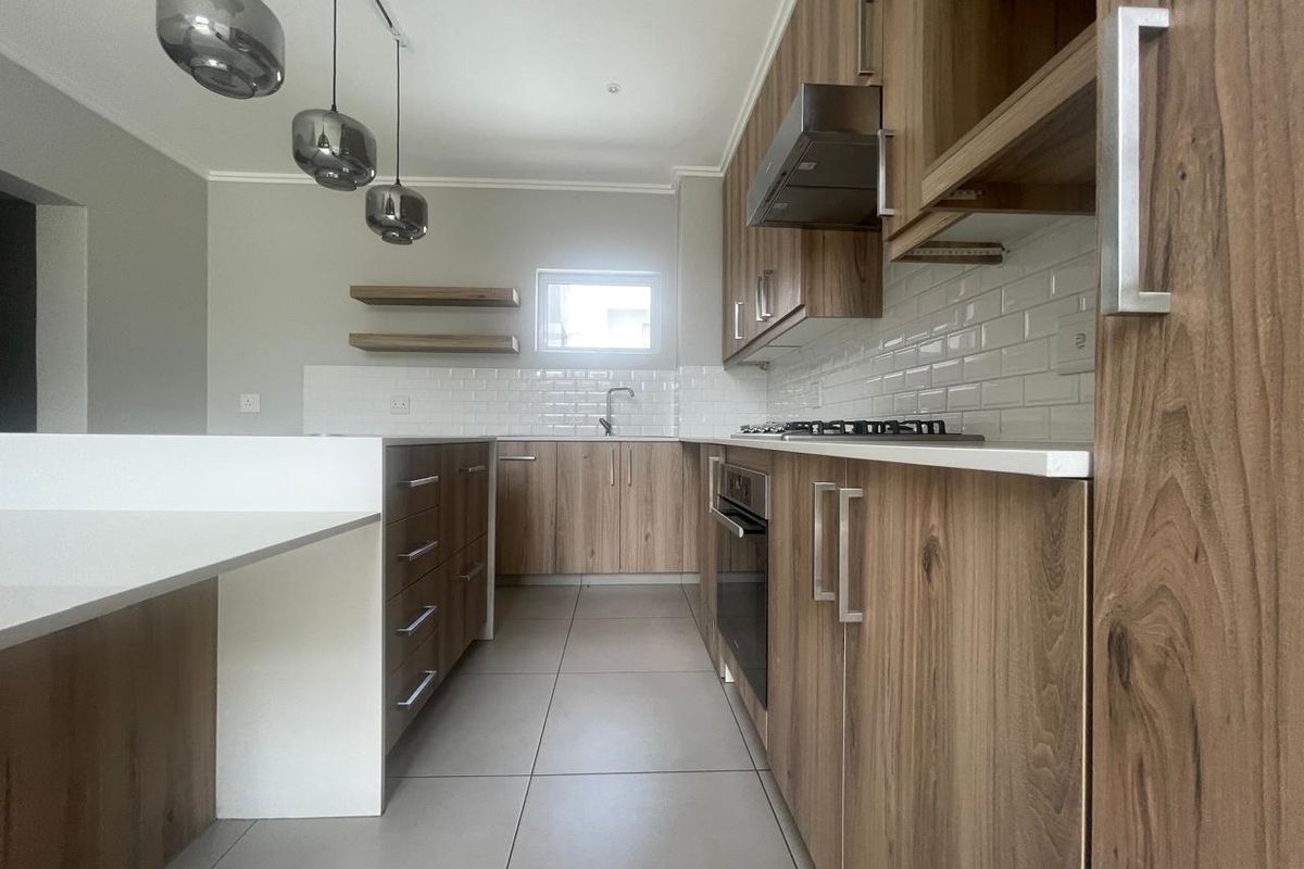Modern kitchen featuring wood-grain cabinetry, white stone countertops, subway tile backsplash, built-in oven, gas hob, and sleek pendant lighting.