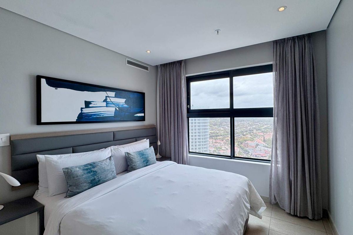 Modern bedroom featuring a large window with city views, integrated air conditioning, and a neutral color palette.