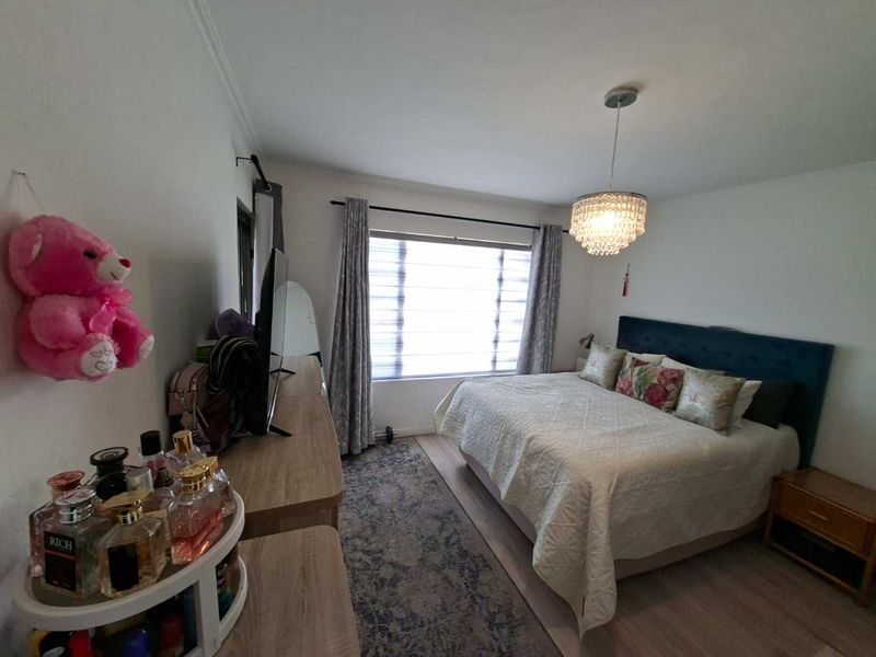 A well-maintained bedroom featuring laminate flooring, a decorative crystal chandelier, and window blinds, offering a comfortable and functional living space.
