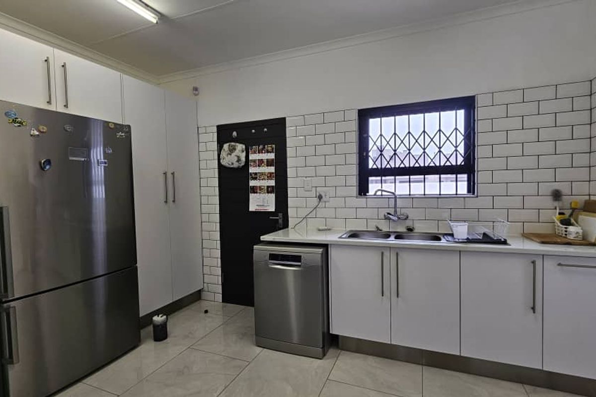 Modern kitchen featuring white cabinetry, subway tile backsplash, stainless steel appliances, and a double basin sink with a security-grilled window.