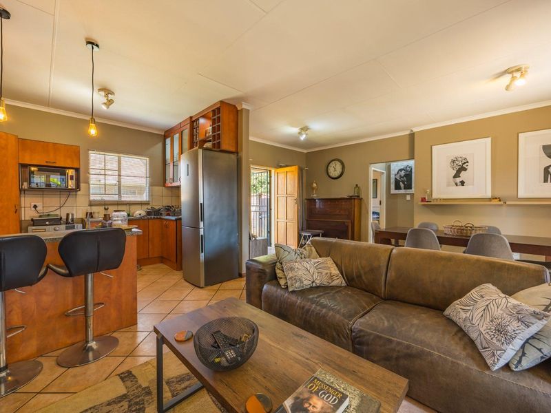 Open-plan living and kitchen area featuring tiled floors, wooden cabinetry, a breakfast bar, and integrated kitchen appliances.