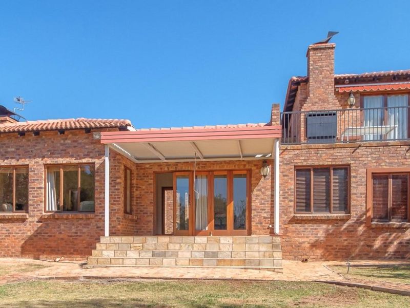 Rear view of a double-story brick house featuring a covered patio, stone steps, and an upper-level balcony with a chimney.