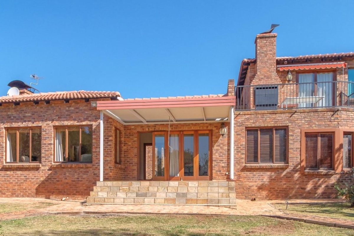 Rear view of a double-story brick house featuring a covered patio, stone steps, and an upper-level balcony with a chimney.