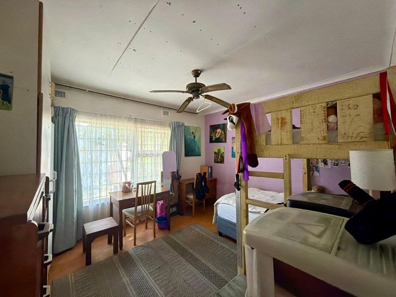 A bedroom featuring a ceiling fan and large window with security gate. The room requires cosmetic updates to the ceiling and wall finishes.