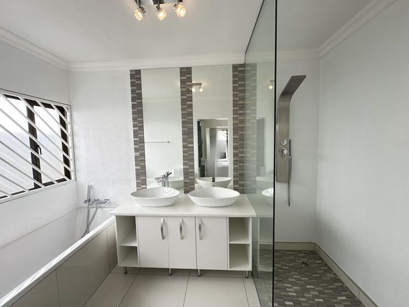 Modern bathroom featuring a double vanity with vessel sinks, a built-in bathtub, and a spacious glass-enclosed shower with a contemporary shower panel.