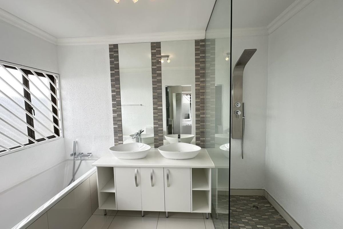Modern bathroom featuring a double vanity with vessel sinks, a built-in bathtub, and a spacious glass-enclosed shower with a contemporary shower panel.