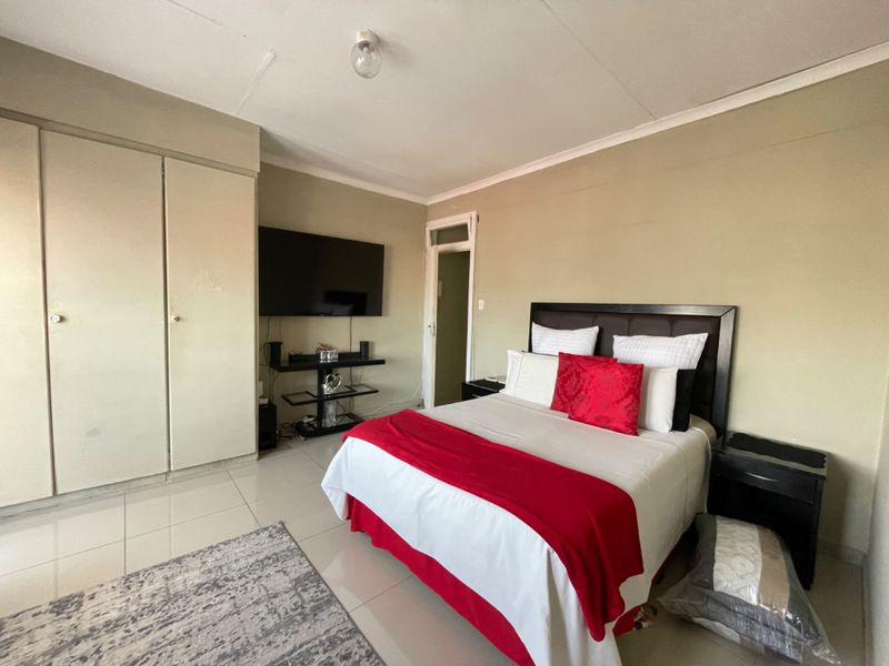 A functional bedroom featuring tiled flooring, built-in cupboards, and a coved ceiling, offering a neutral base for potential interior updates.