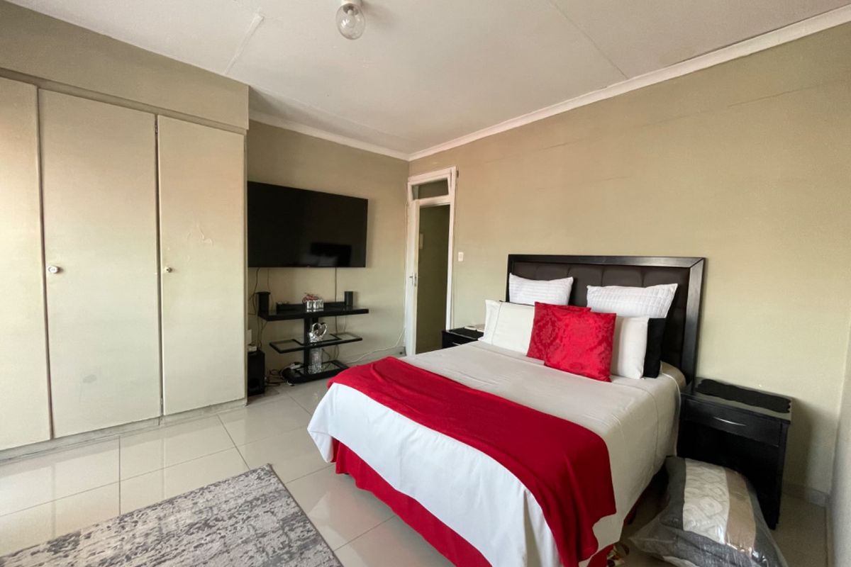 A functional bedroom featuring tiled flooring, built-in cupboards, and a coved ceiling, offering a neutral base for potential interior updates.