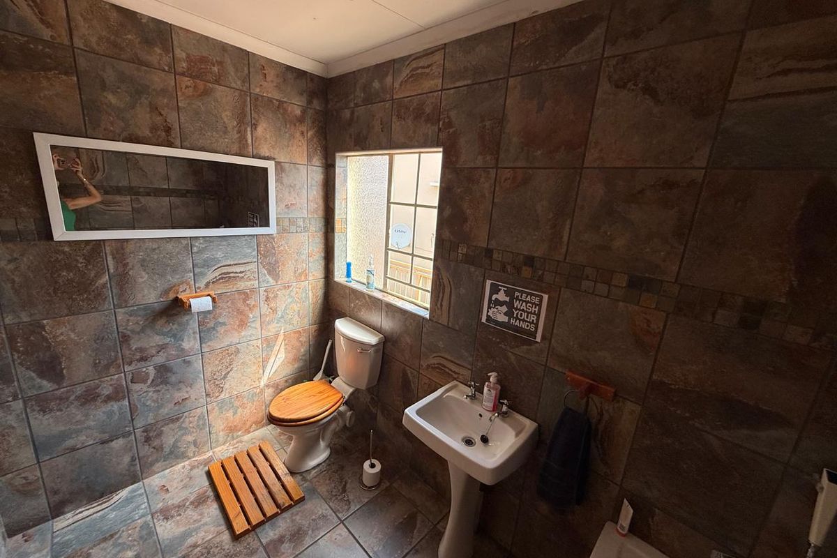A functional bathroom featuring full-height stone-look wall tiling, a pedestal basin, and a standard toilet with a wooden seat.