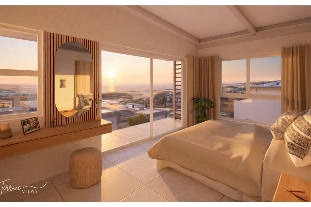 A modern bedroom featuring large sliding glass doors that open to a balcony with expansive coastal sunset views.