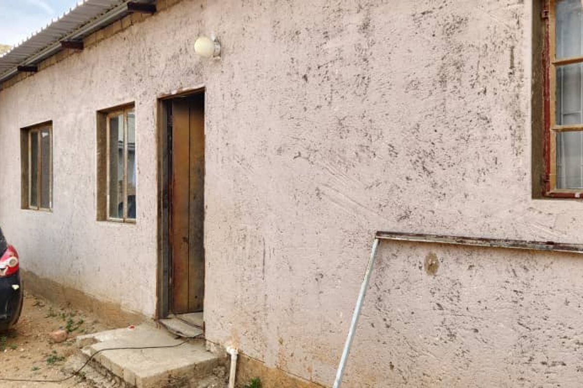 Rear exterior view of the property featuring textured plaster walls, steel-framed windows with security bars, and a corrugated metal roof overhang.