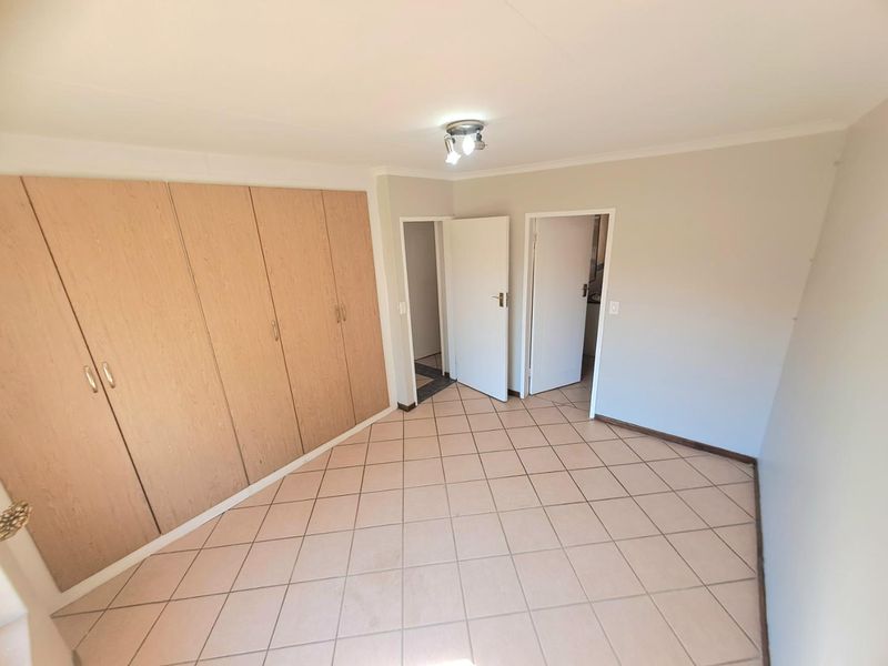 A vacant bedroom featuring neutral tiled flooring and extensive built-in wooden cupboards, offering a clean and functional space ready for personalization.