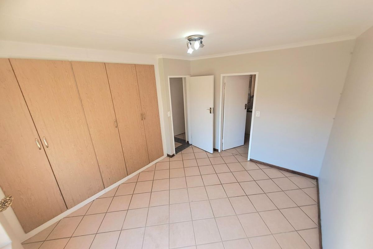 A vacant bedroom featuring neutral tiled flooring and extensive built-in wooden cupboards, offering a clean and functional space ready for personalization.