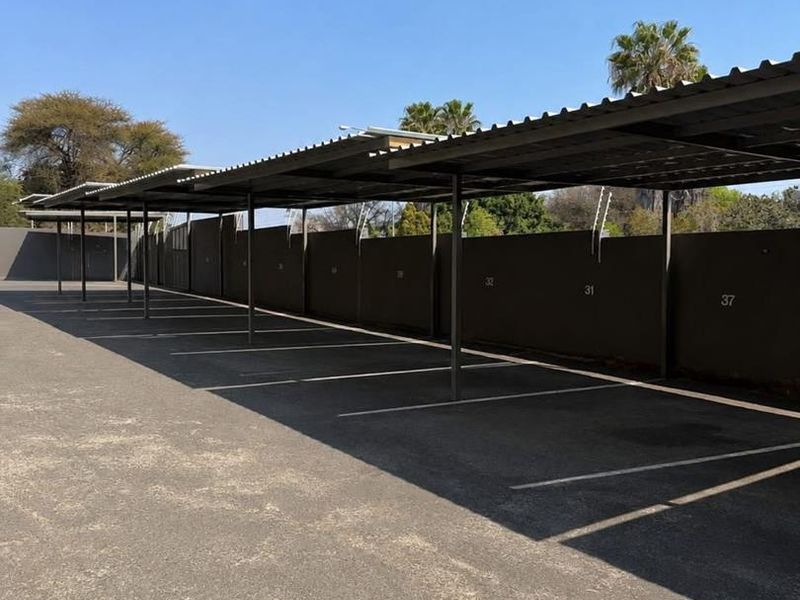 A row of covered, numbered parking bays featuring a metal roof structure and asphalt paving within a secure complex.